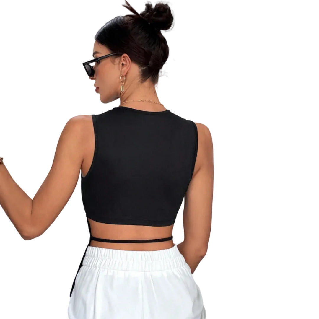 Woman wearing a black crop top and white pants against a plain background