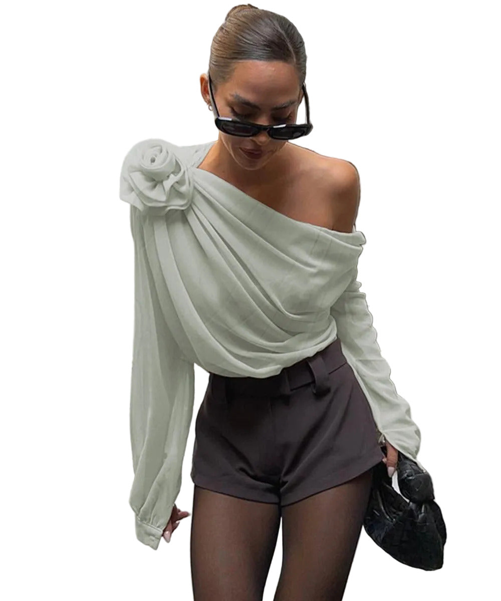 Woman wearing a light green off-shoulder top and brown shorts, standing indoors.