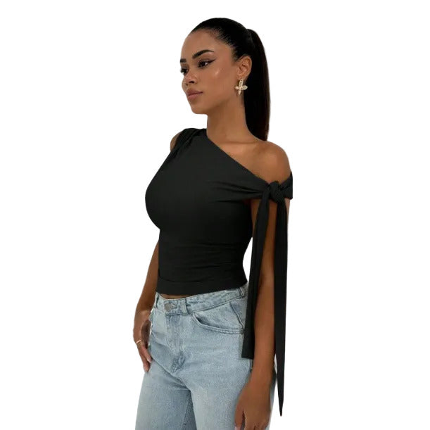 Woman wearing a black one-shoulder top with a tie detail and light blue jeans against a white background