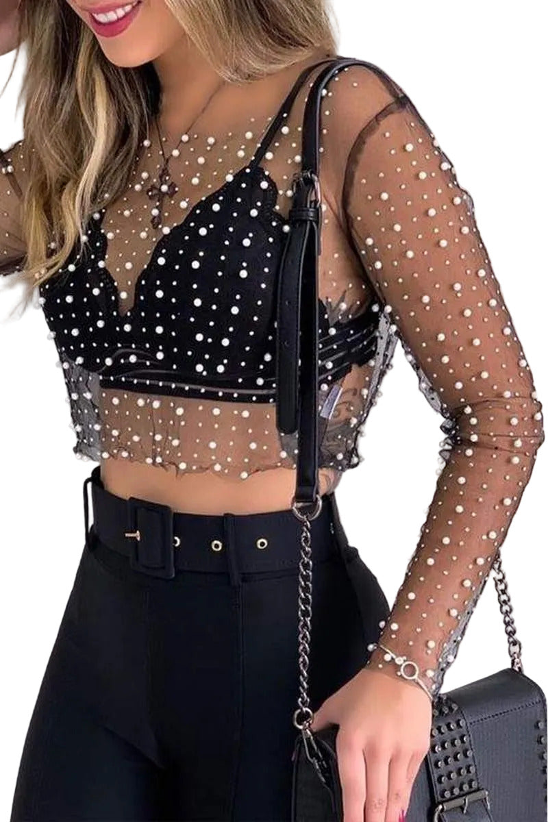 Woman wearing a black sheer top with white polka dots and black pants, holding a black handbag.