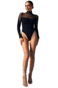 Model wearing a black bodysuit and sheer thigh-high stockings against a gray background