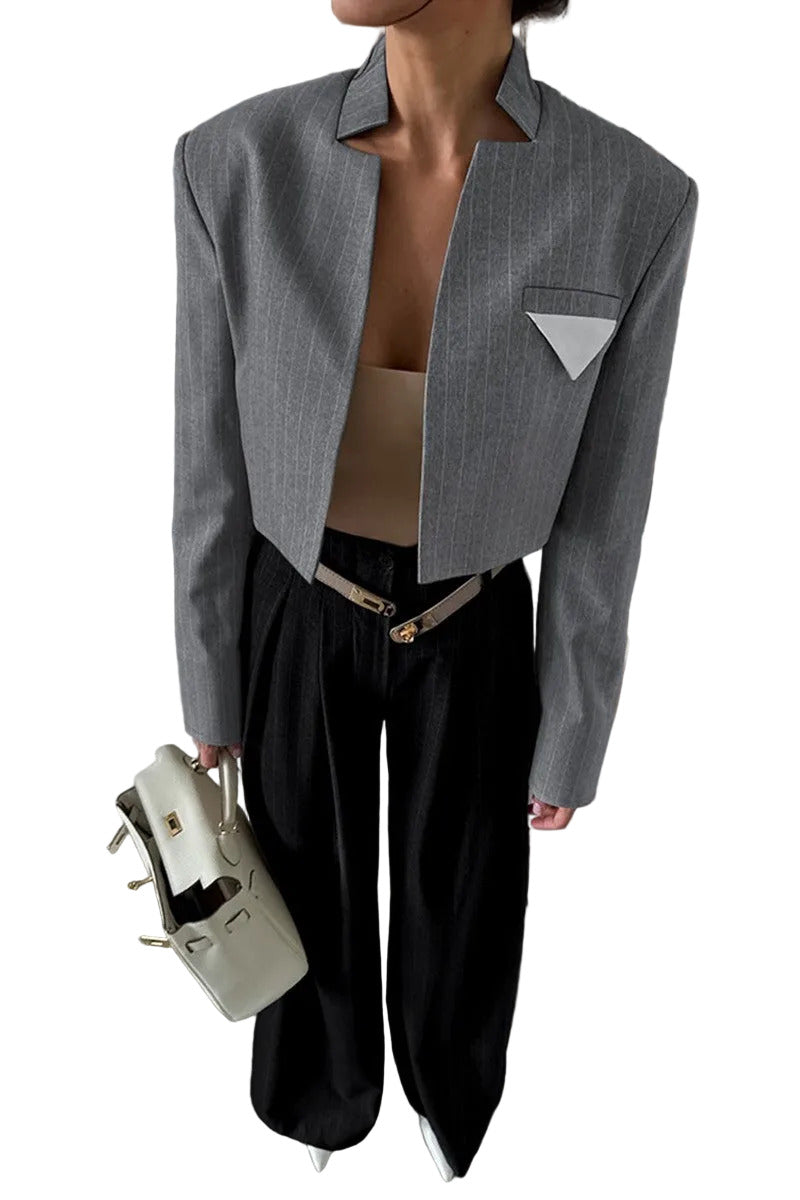 Person wearing a gray blazer and black pants holding a beige handbag in a room with bookshelves.