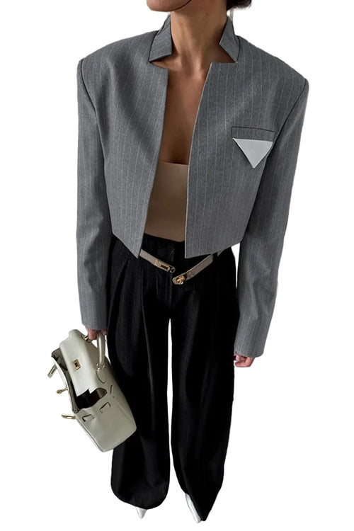 Person wearing a gray blazer and black pants holding a beige handbag in a room with bookshelves.
