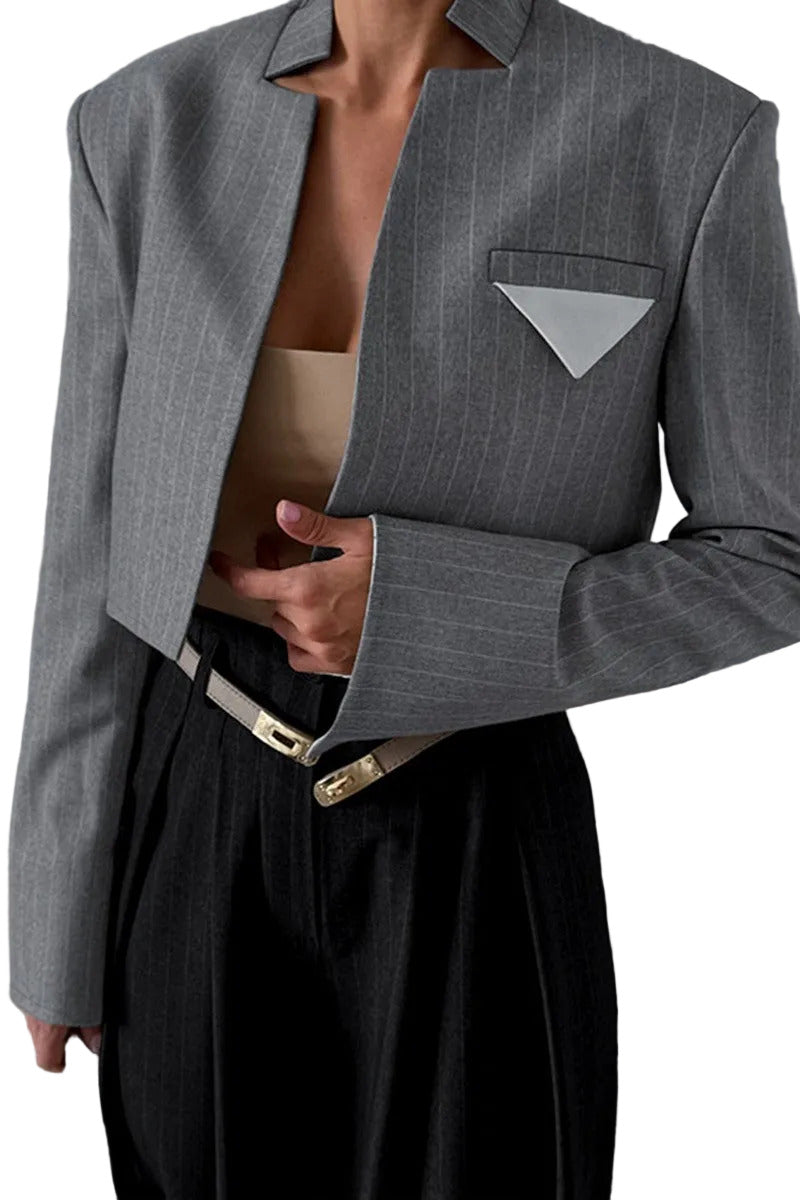 Person wearing a gray pinstripe blazer over a black outfit with a blurred background.