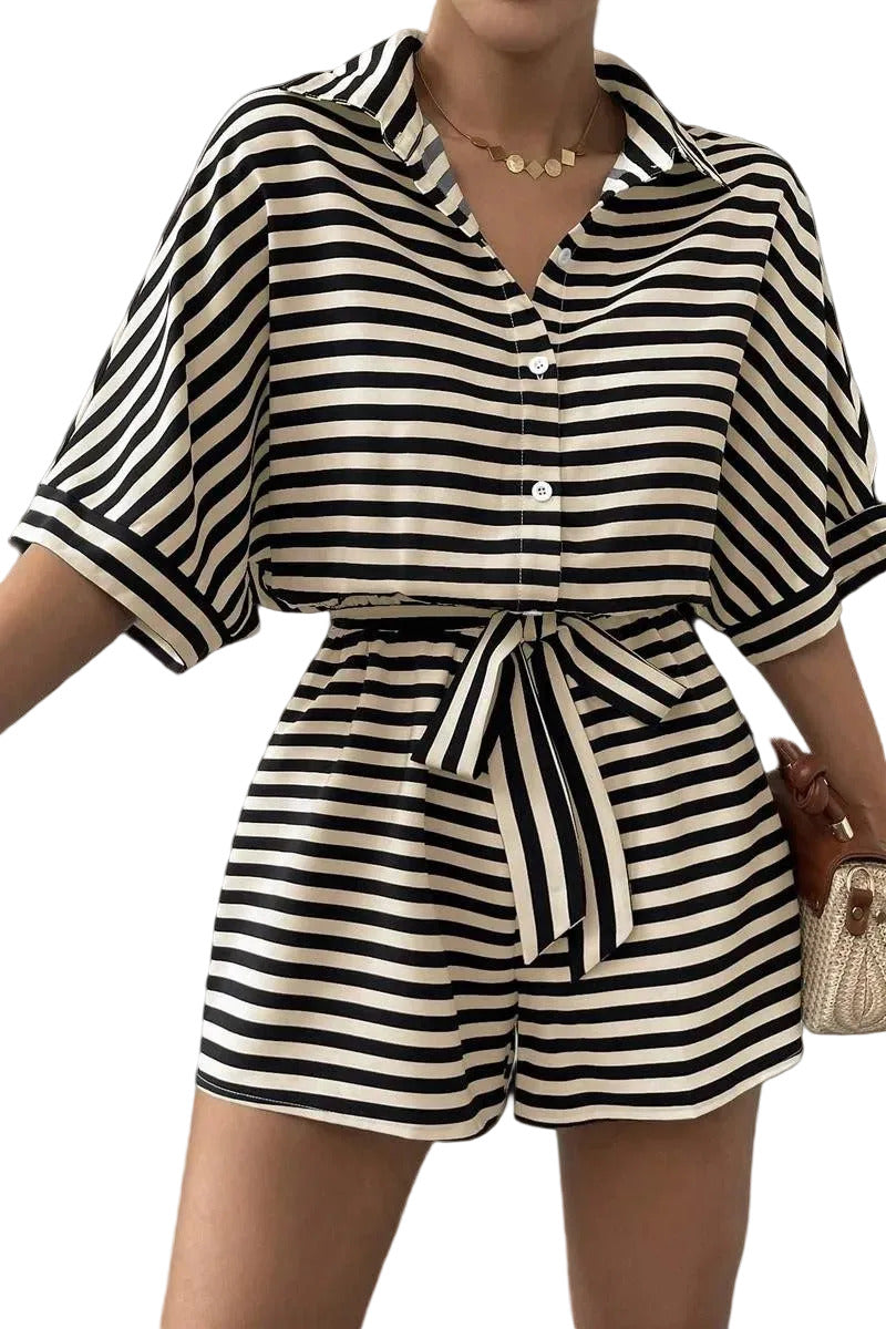 Person wearing a black and white striped romper with a belt on a gray background