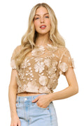 Woman wearing a beige floral lace top and light blue jeans indoors.