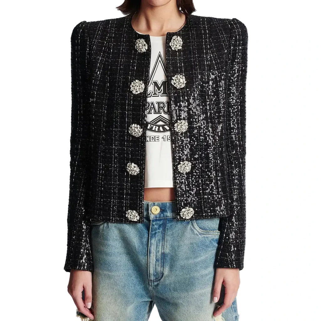 Person wearing a black sequin jacket over a white graphic t-shirt and blue jeans on a light gray background