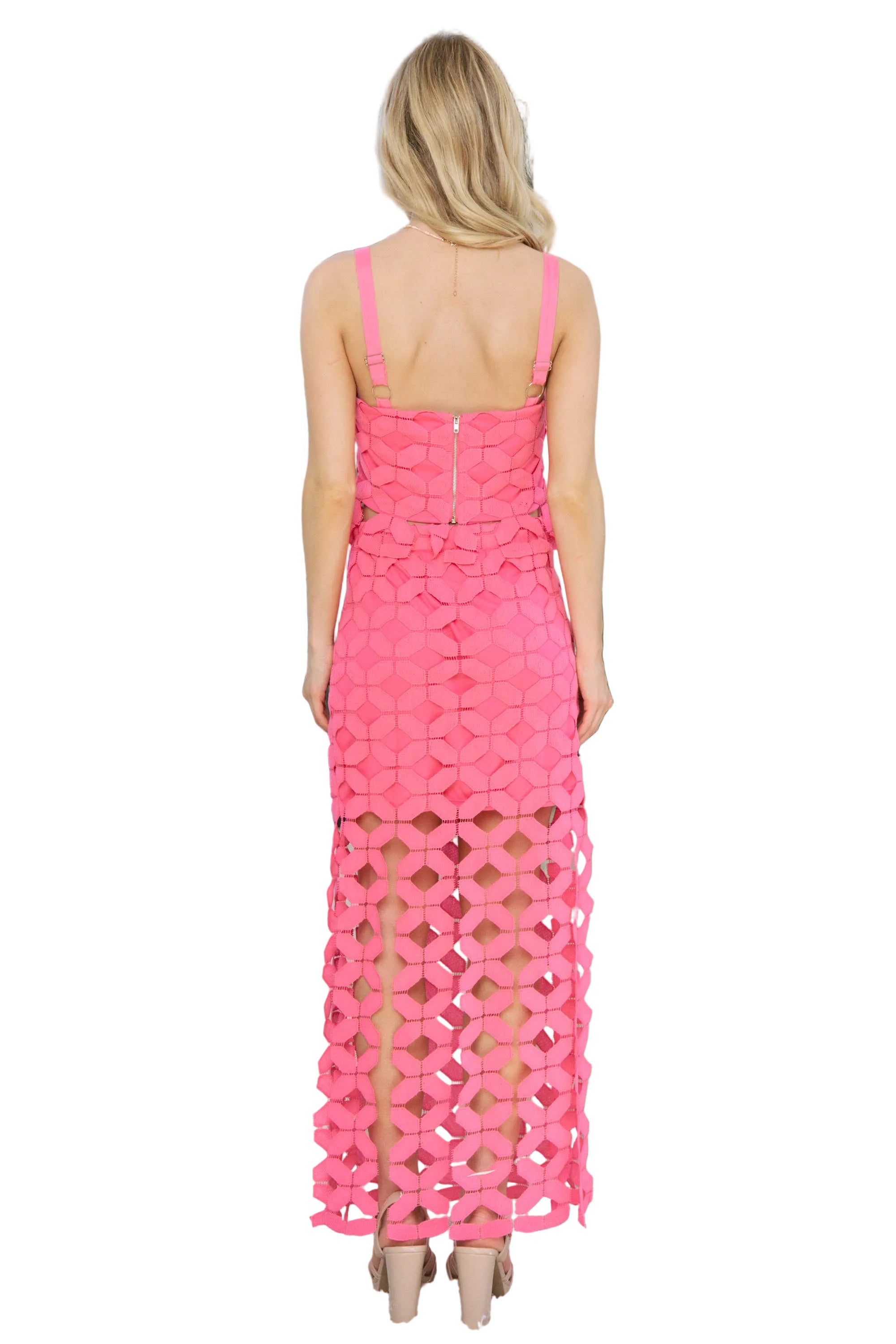 Woman wearing a pink tank top and matching skirt with cut-out patterns standing.