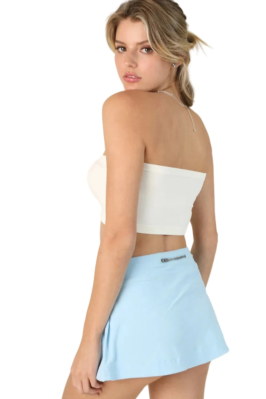 Woman wearing a white strapless top and light blue skirt on a beige background